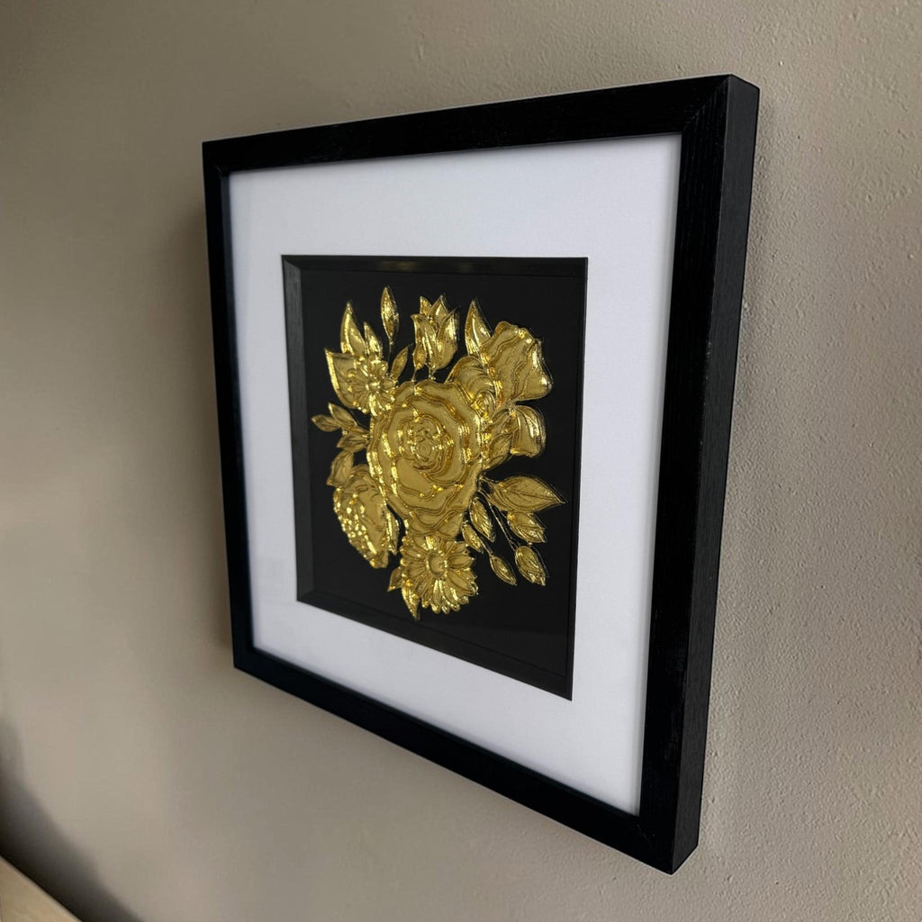 Angled wall display of framed gold-finish floral bouquet relief with wide white mount and black box frame.