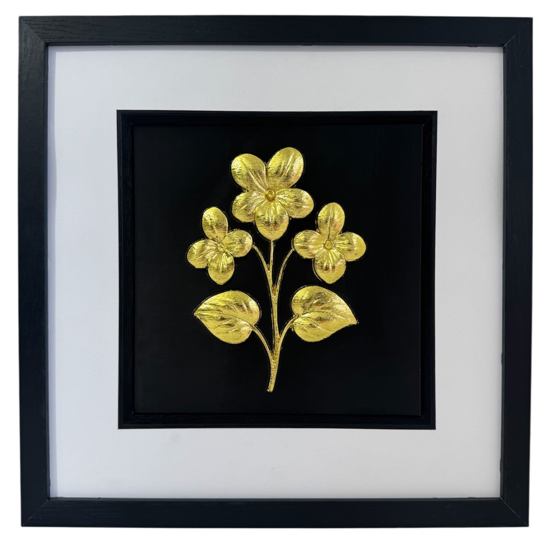 Gold framed floral relief with three flowers and two leaves on a black background with a wide white mount and black inner surround