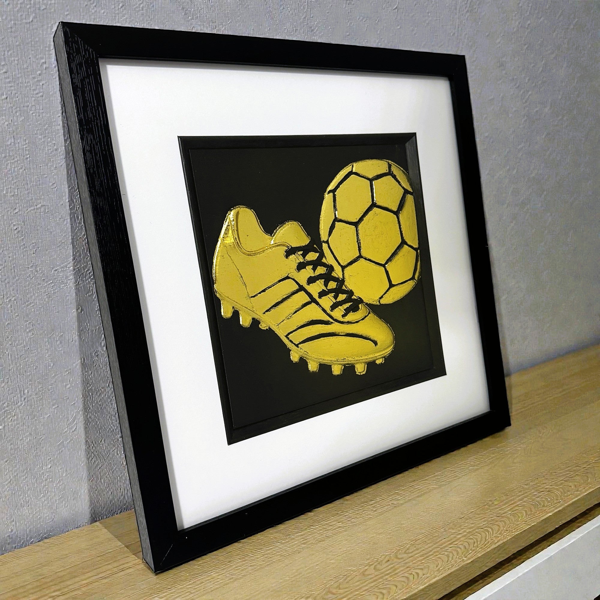 Framed gold football art displayed on shelf for bedroom decor.