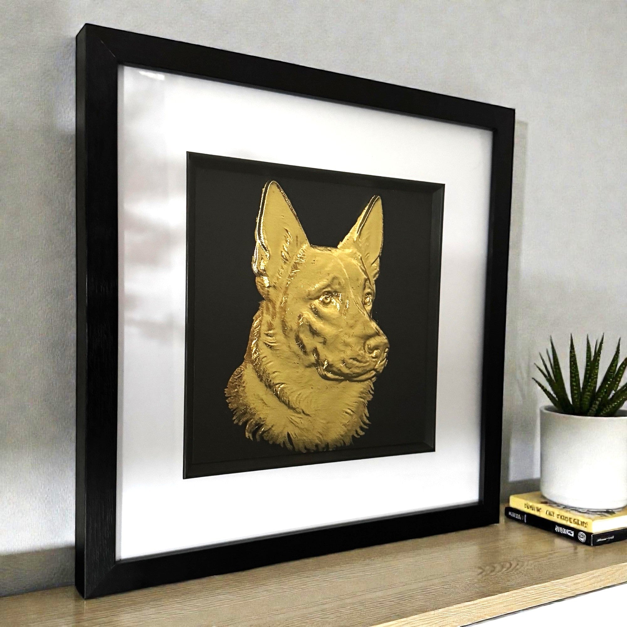 German Shepherd framed wall art in gold leaf viewed at an angle, displayed in a black wooden frame with white mount
