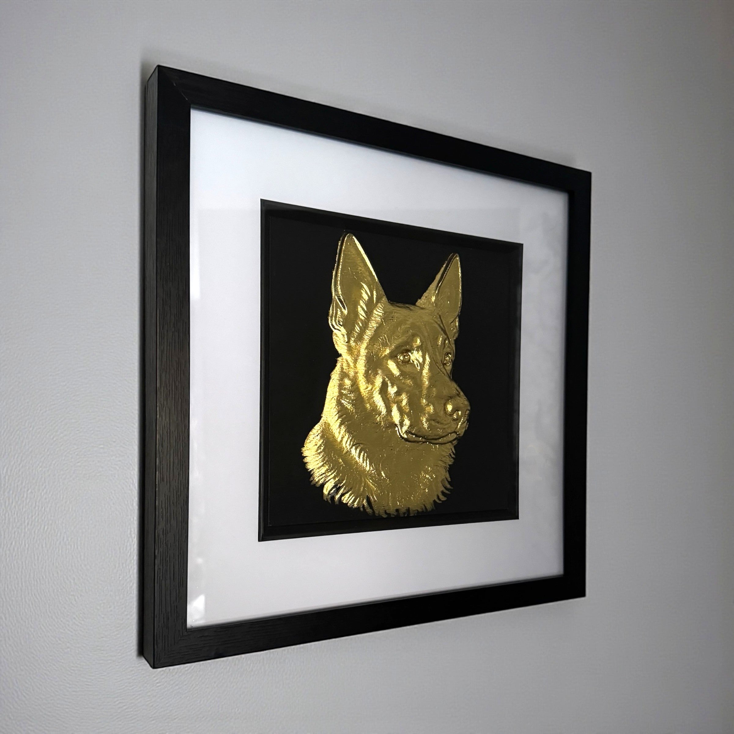 German Shepherd framed wall art in gold leaf mounted on a wall, with black wooden frame, white mount, and black background
