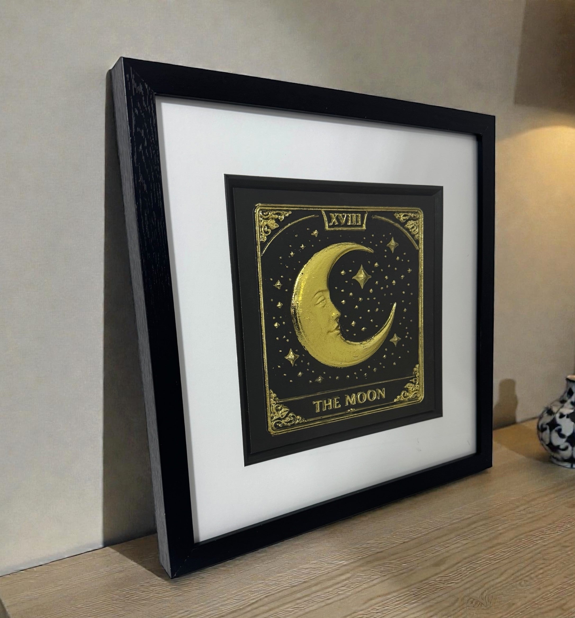 The Moon tarot card 3D wall art in gold leaf on wooden surface, framed in black with white mount, mystical decor lifestyle photo