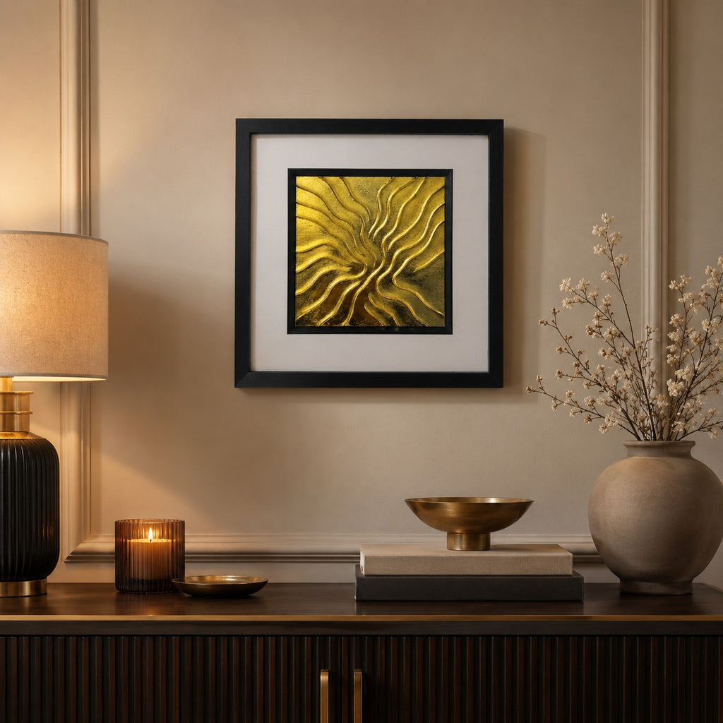 Gold abstract flow wall art in a black square frame styled above a dark wood console with warm lighting, brass decor and neutral modern luxury interiors.