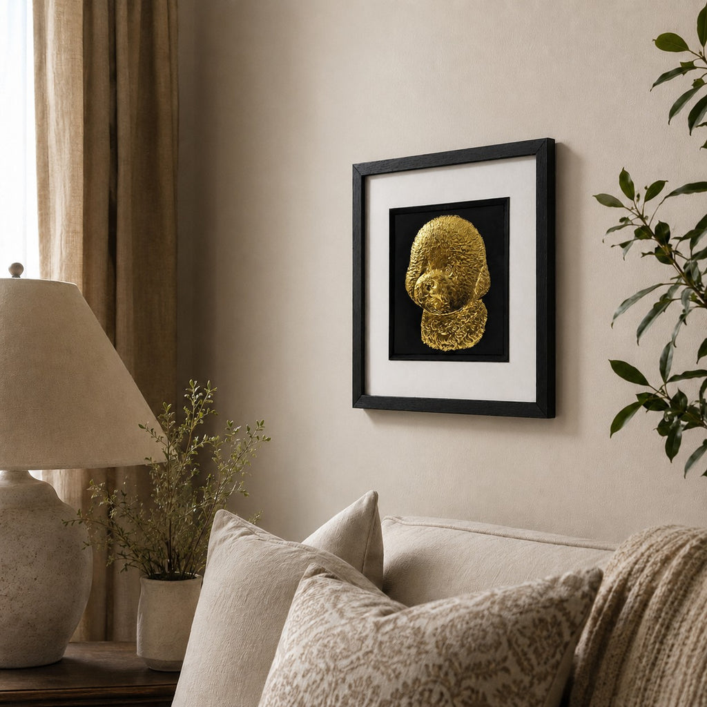 Angled lifestyle view of gold Bichon Frise framed wall art hung on a neutral wall above a cosy sofa with soft decor and greenery.