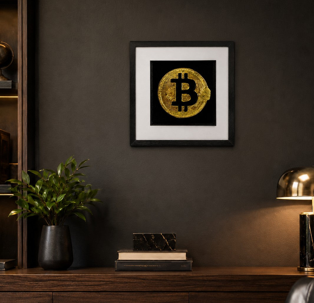 Framed gold Bitcoin wall art on a dark textured wall above a wooden console, styled with a plant, books and a modern lamp in a luxury home office setting.