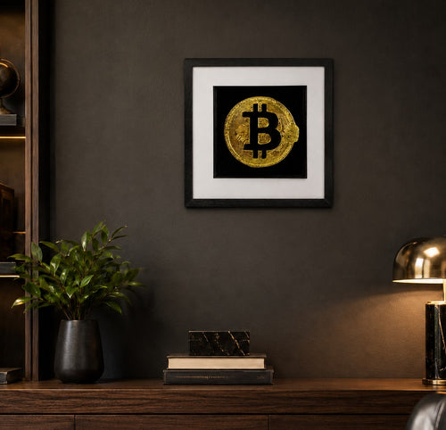 Framed gold Bitcoin wall art on a dark textured wall above a wooden console, styled with a plant, books and a modern lamp in a luxury home office setting.