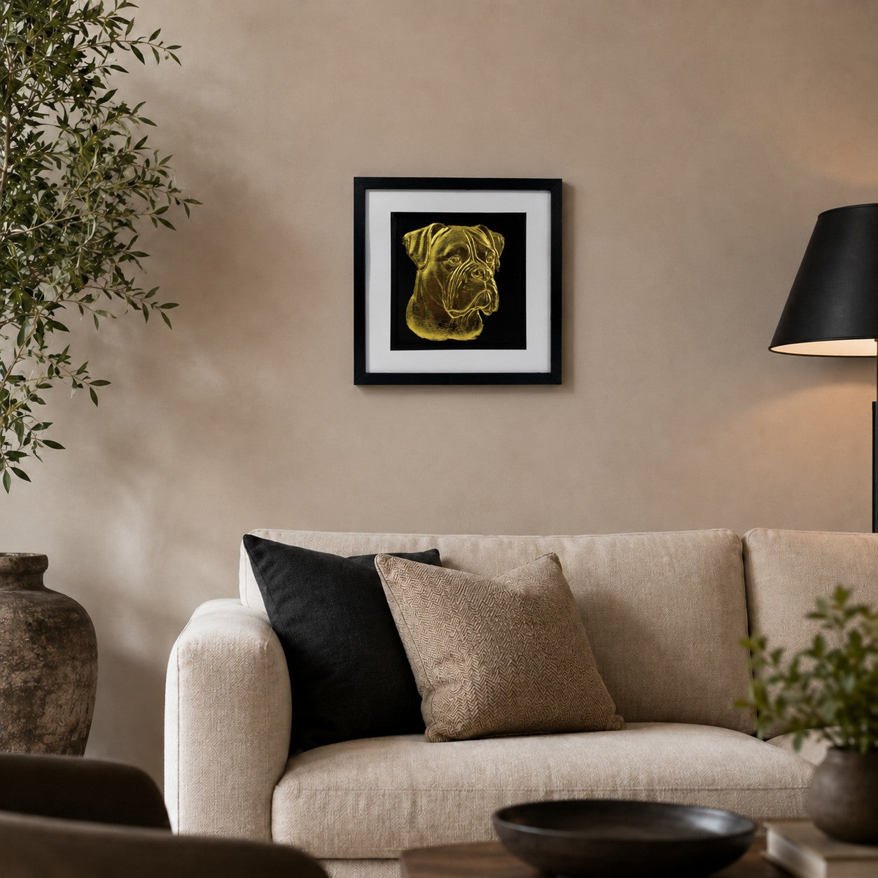 Gold Boxer dog 3D wall art in a black frame displayed on a warm neutral living room wall above a cream sofa with black accents and greenery.