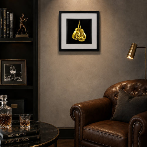 Framed gold boxing gloves wall art displayed in a dark luxury lounge with leather chair, boxing decor and warm lighting, ideal for sports decor or boxing gift.