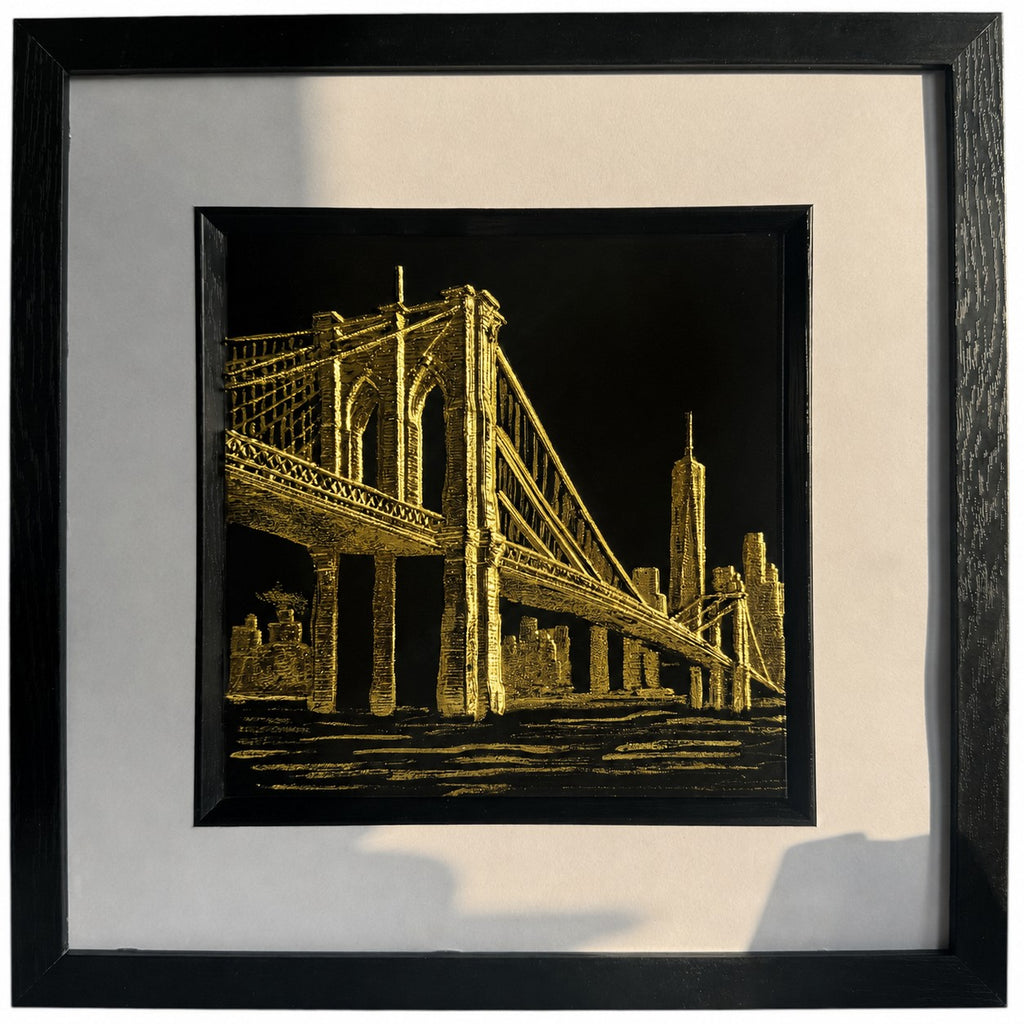 Gold Brooklyn Bridge New York wall art in a black frame with white mount, featuring a hand gilded gold leaf 3D relief bridge and city skyline design on a black background.