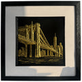 Gold Brooklyn Bridge New York wall art in a black frame with white mount, featuring a hand gilded gold leaf 3D relief bridge and city skyline design on a black background.