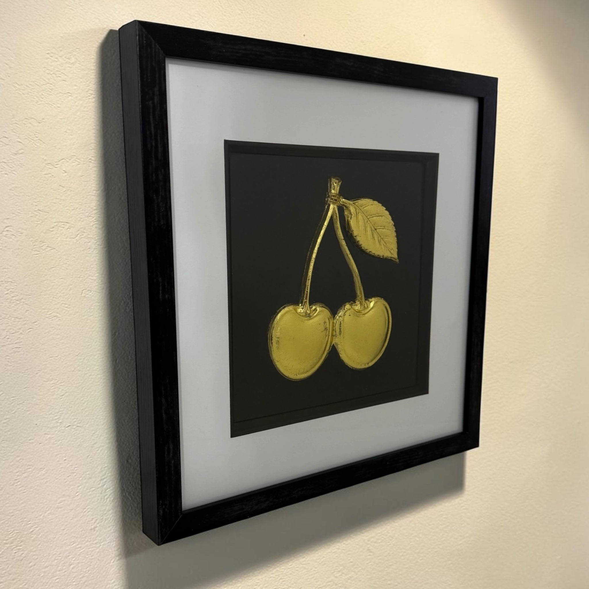 Gold cherry relief kitchen wall art on a neutral wall with black centre panel and white mount.