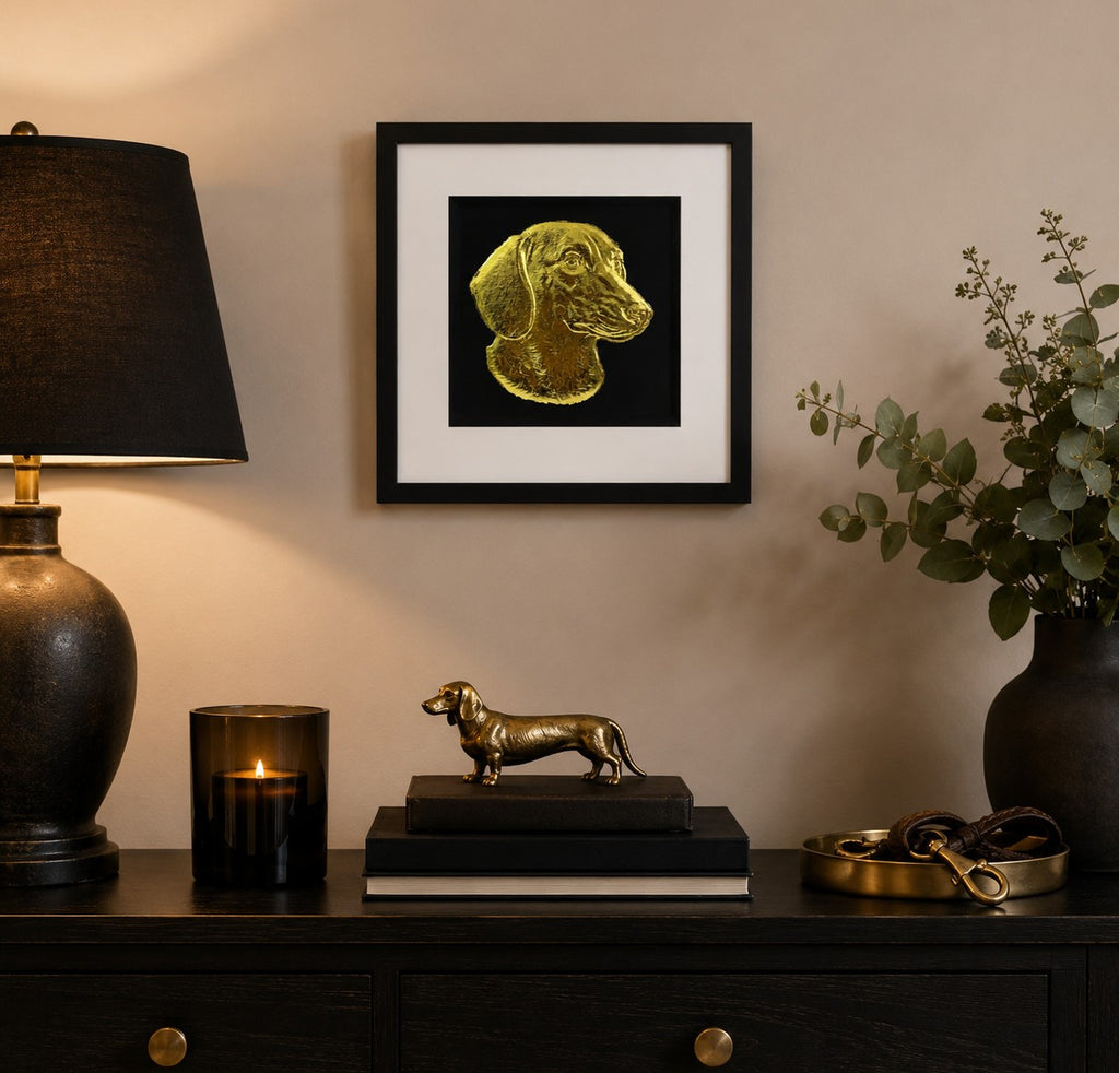 Framed gold Dachshund sausage dog wall art on a black background, styled in a warm modern dog lover home interior with black, gold and neutral decor accents.