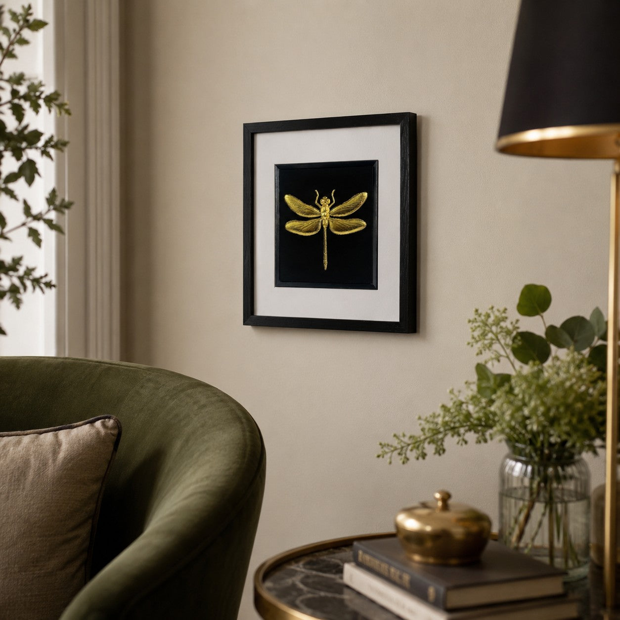 55 degree angled view of framed gold dragonfly wall art in a black square frame with white mount, hanging on a neutral wall in a refined living room setting.
