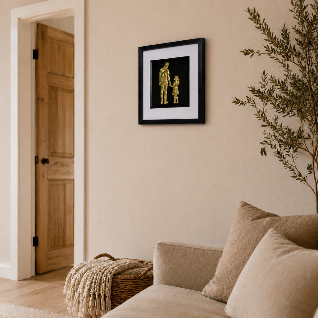 Angled lifestyle view of gold father and daughter wall art mounted on a neutral living room wall beside a sofa and natural home décor.