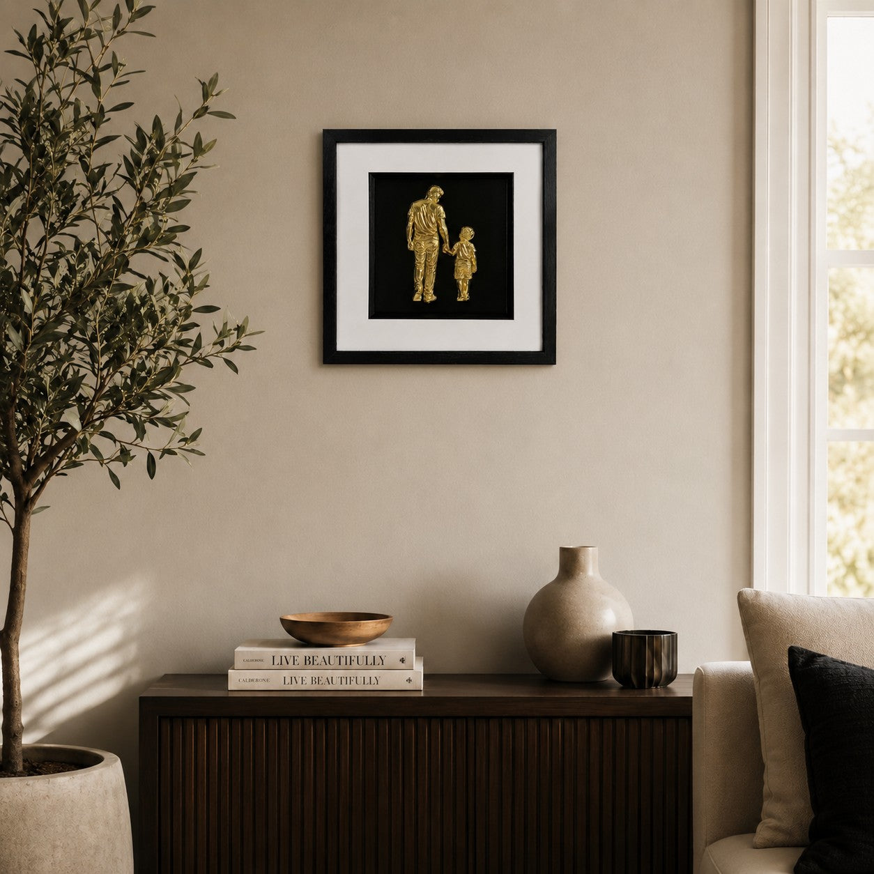 Gold father and son framed artwork above a wooden sideboard with plant, vase and neutral styling.