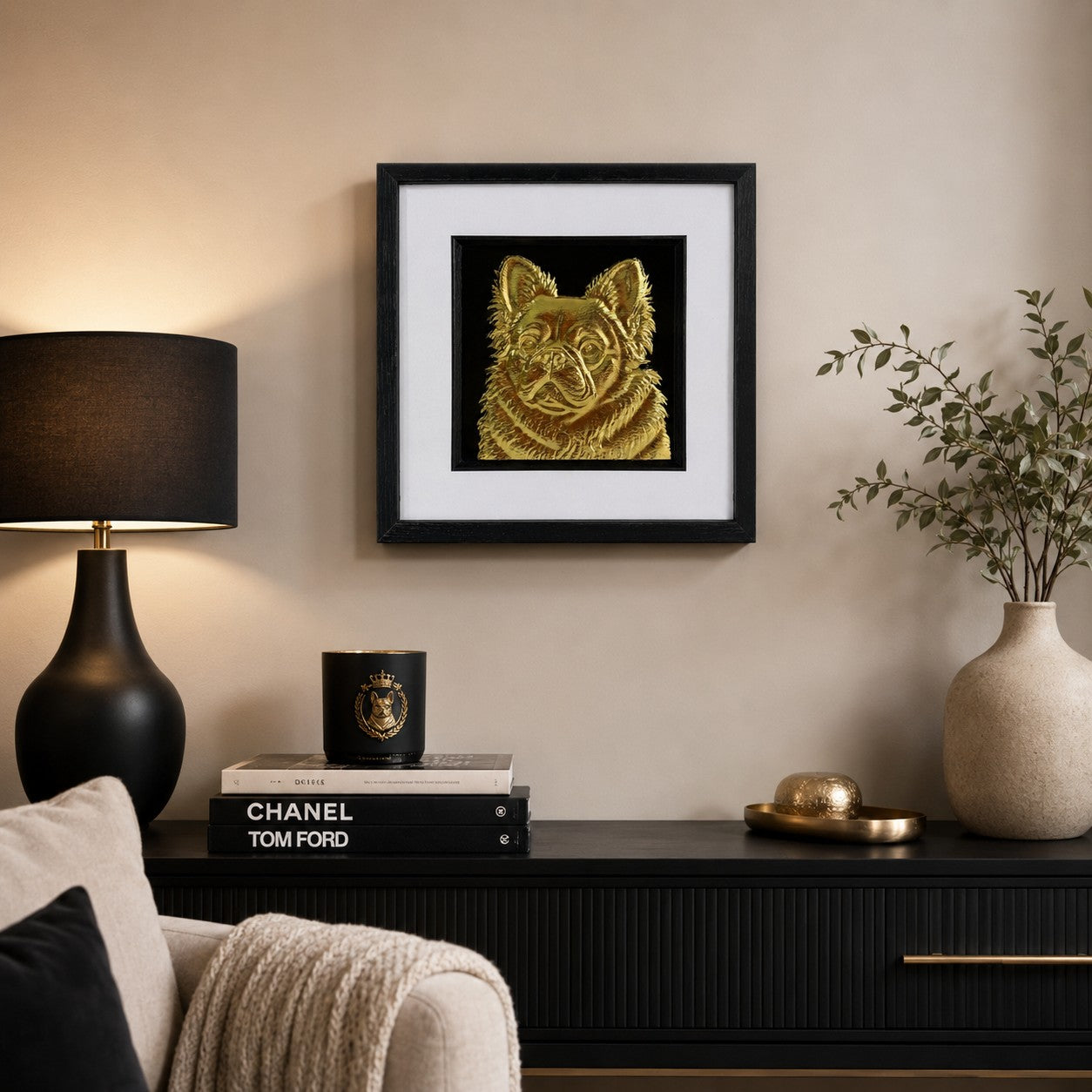 Gold fluffy French Bulldog relief artwork in a black square frame styled above a dark sideboard with lamp and neutral decor.