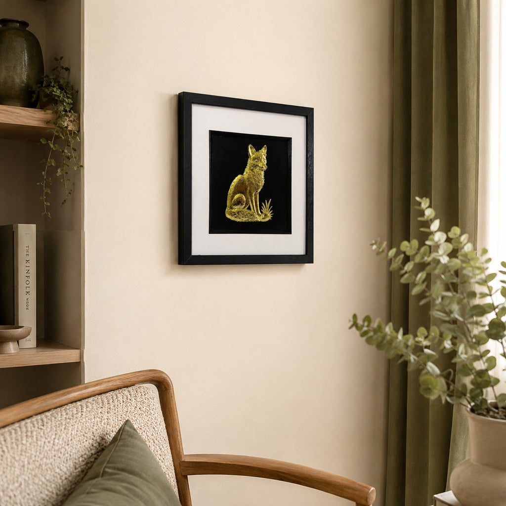 Angled lifestyle view of gold fox framed wall art hung on a neutral wall in a calm woodland-inspired interior with plants, wood tones and sage green decor.