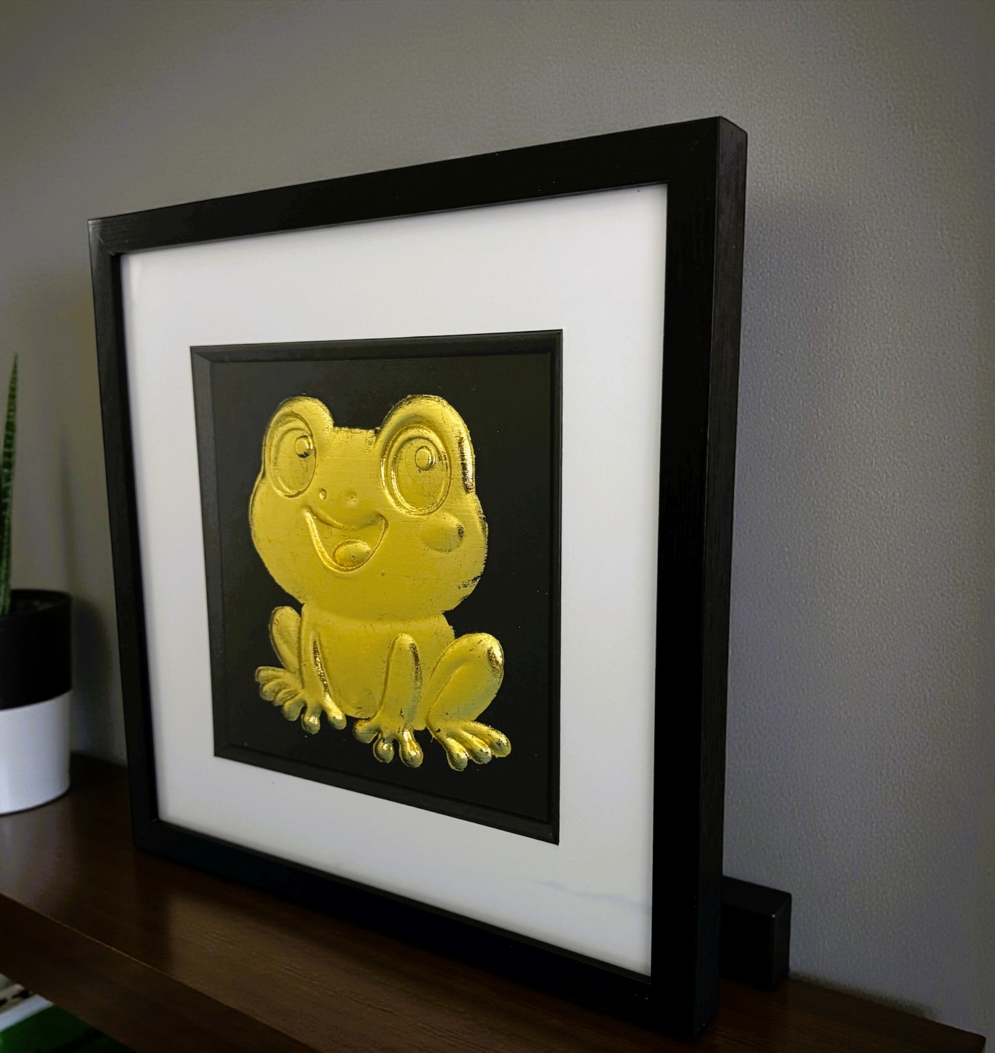 Gold frog 3d wall art framed on dark wooden sideboard