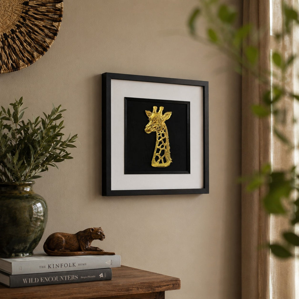 Angled lifestyle view of gold giraffe framed wall art hung on a neutral wall beside natural decor, greenery and warm earthy interior styling.