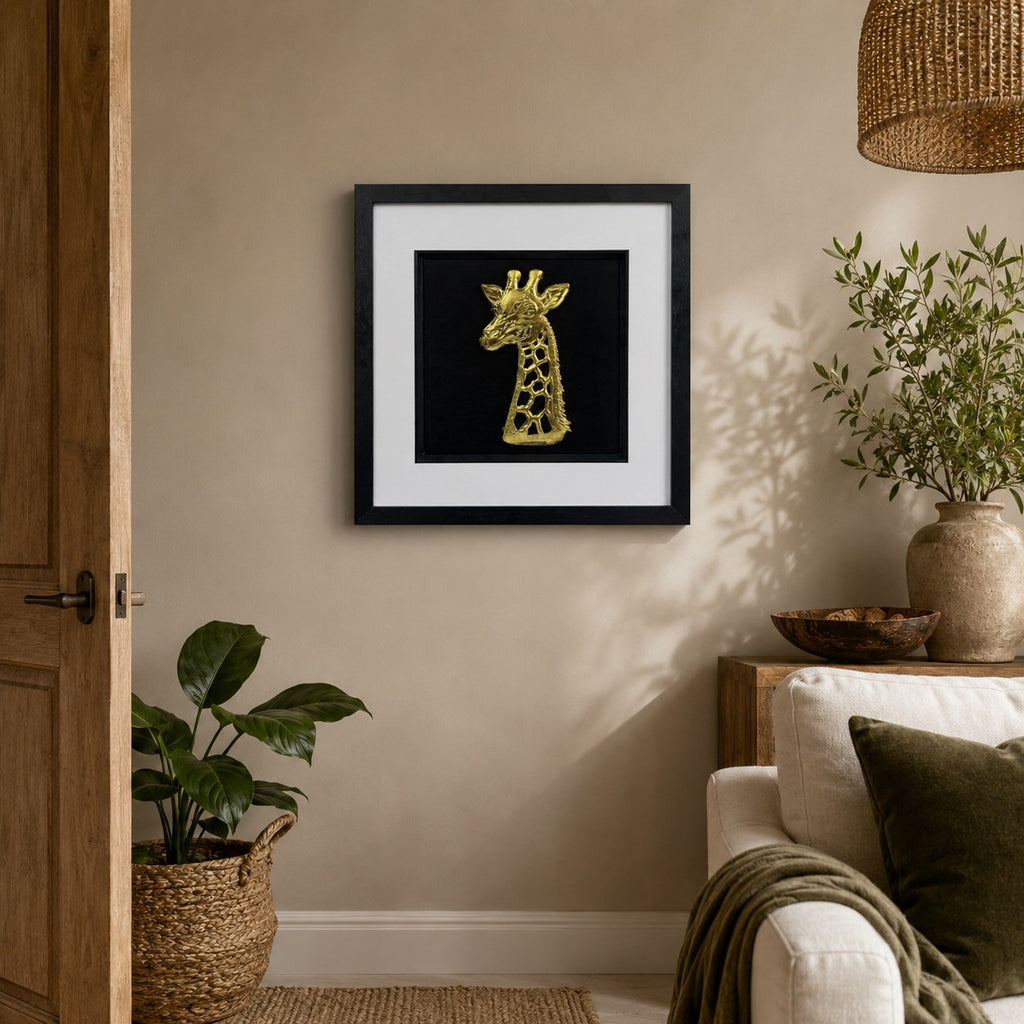 Gold giraffe wall art in a black frame displayed on a warm neutral living room wall with natural wood, soft furnishings and leafy green accents.