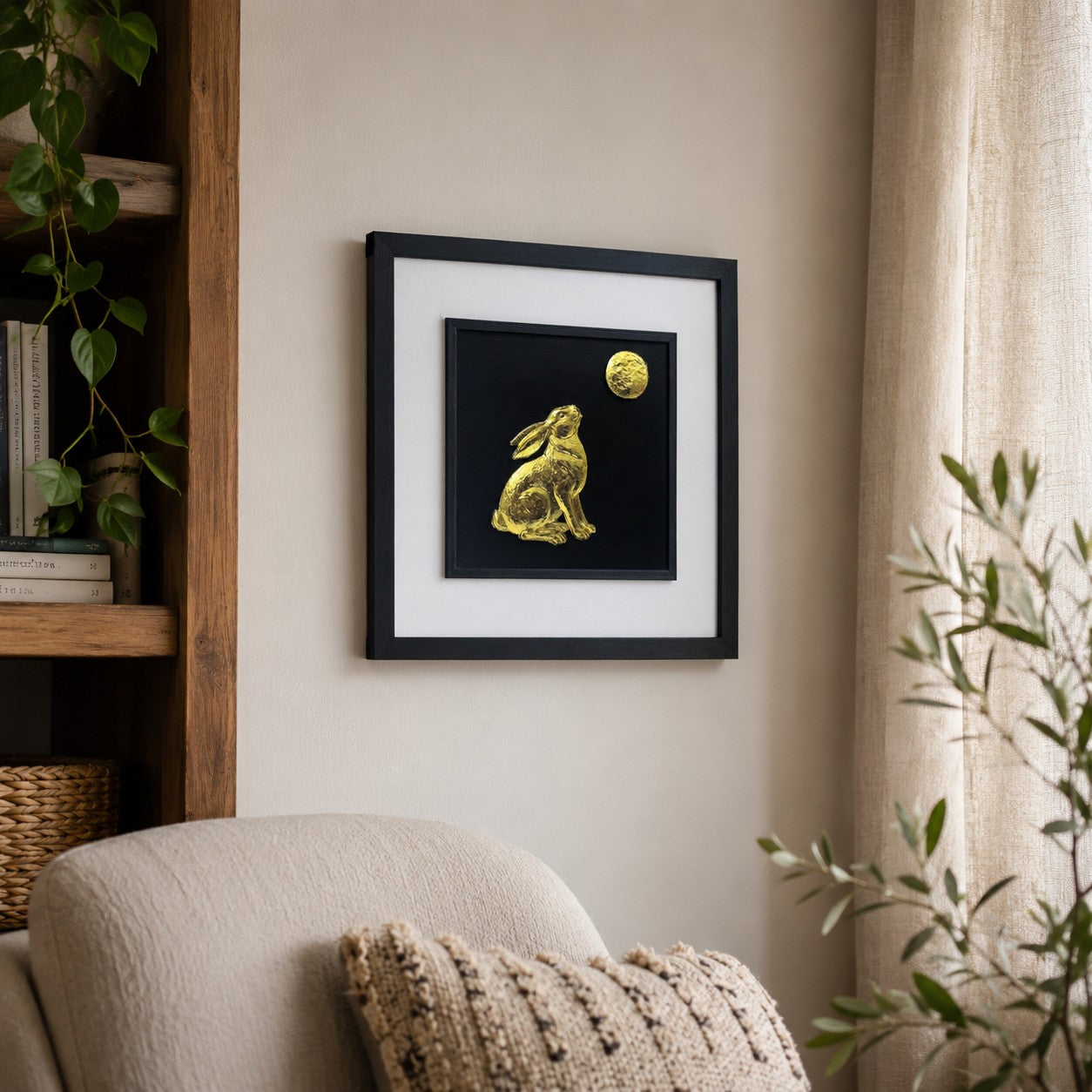 Angled lifestyle view of gold hare gazing at the moon wall art hung on a neutral wall beside natural wood shelving, plants and soft cosy decor.