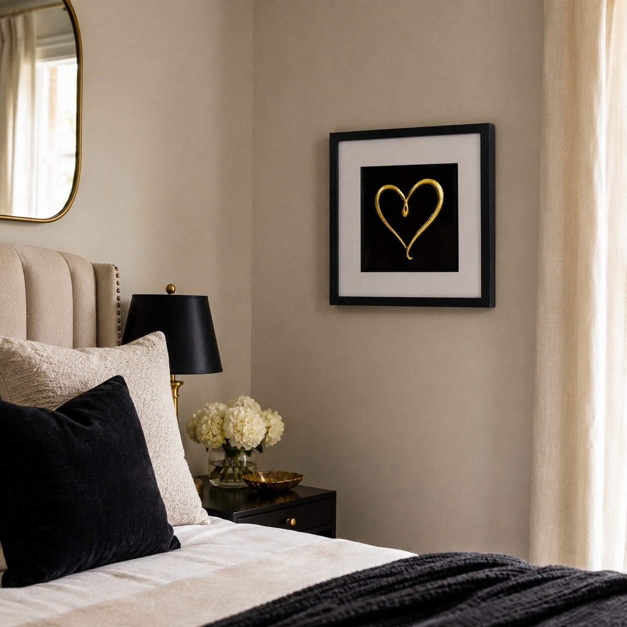 Gold single-line heart 3D artwork in black frame styled on a neutral bedroom wall beside a bed and black lamp.