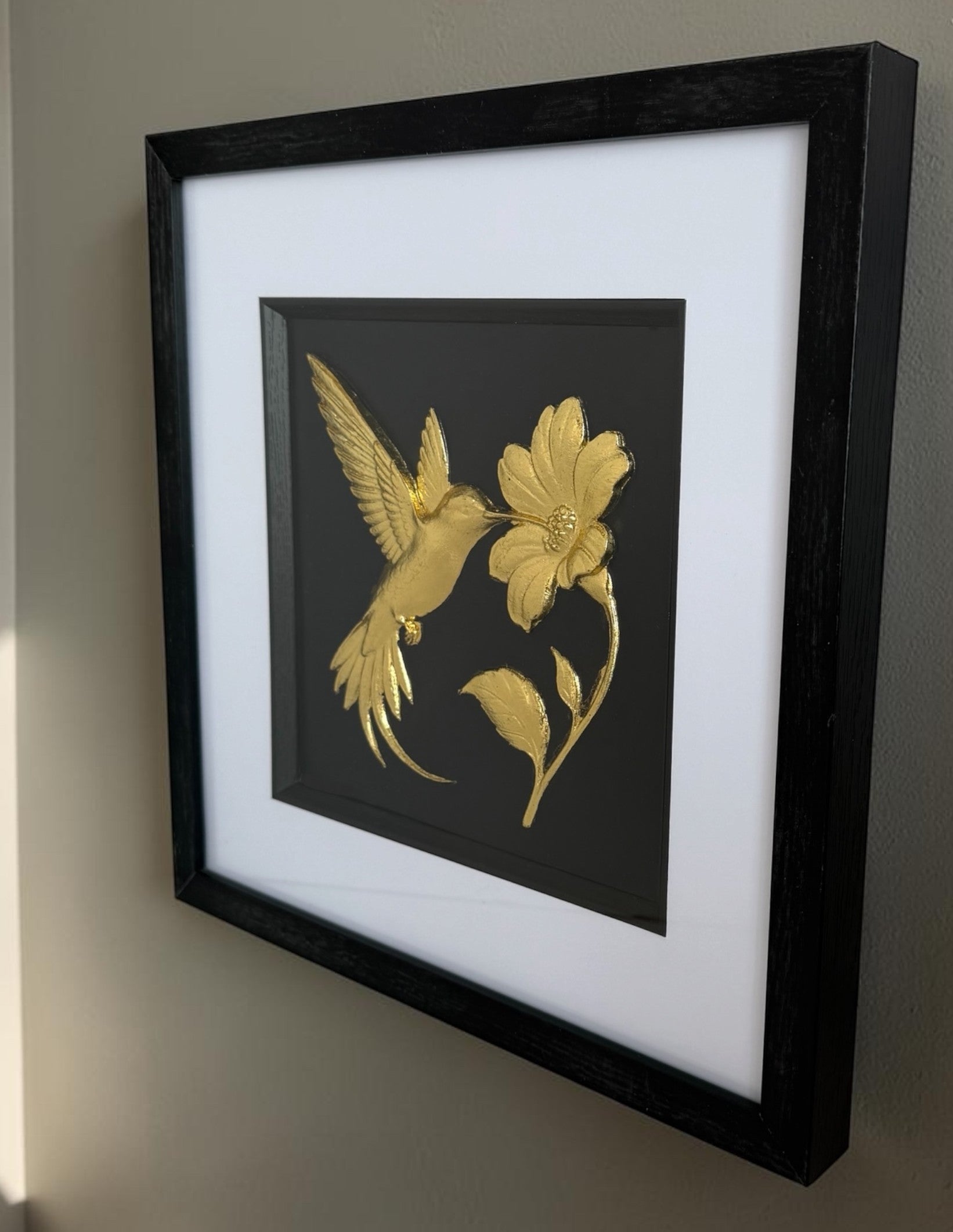 side view gold hummingbird wall art with flower on a wall.