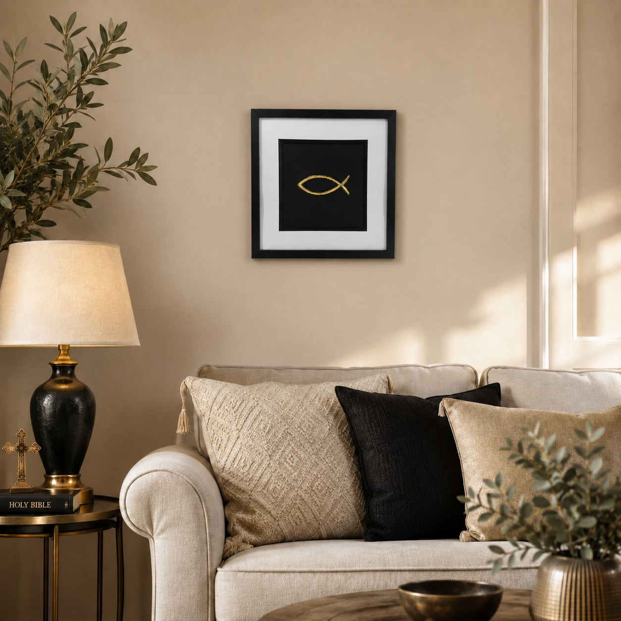 Framed gold Ichthys Christian fish wall art displayed above a neutral living room sofa with black, cream and gold accents.
