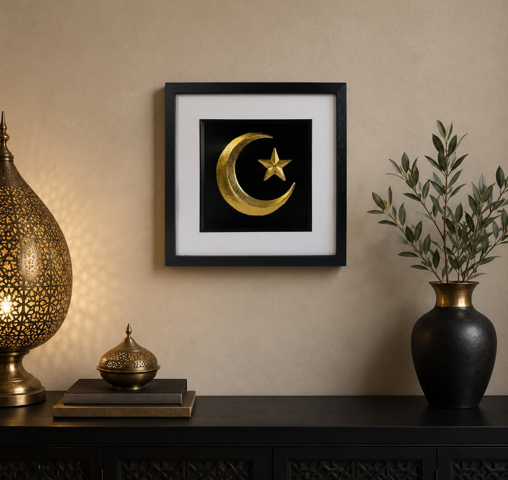 Framed gold Islamic crescent moon and star wall art on a black background, styled in a warm neutral home interior with black and gold decor accents.