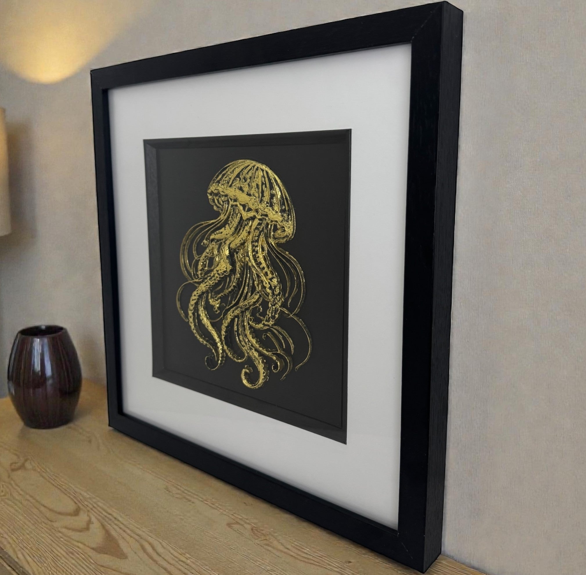 3D jellyfish wall art in gold leaf, framed coastal wall decor with black frame and white mount, styled on an oak sideboard.