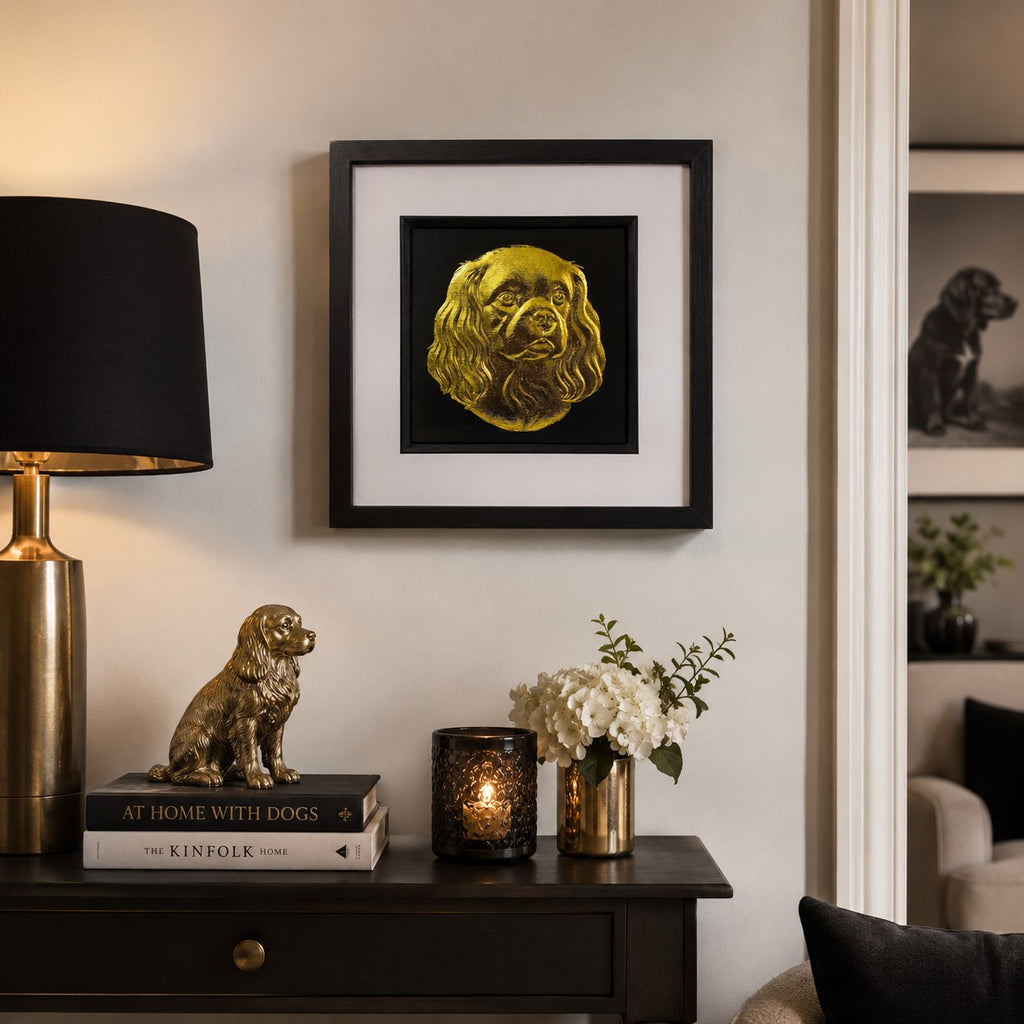 Gold King Charles Spaniel wall art in a black square frame styled above a dark console with dog themed decor, warm lighting and neutral home interiors.
