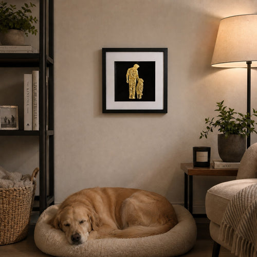Gold finish man and dog artwork styled in a cosy living room above a sleeping dog with warm lamp light and plants.