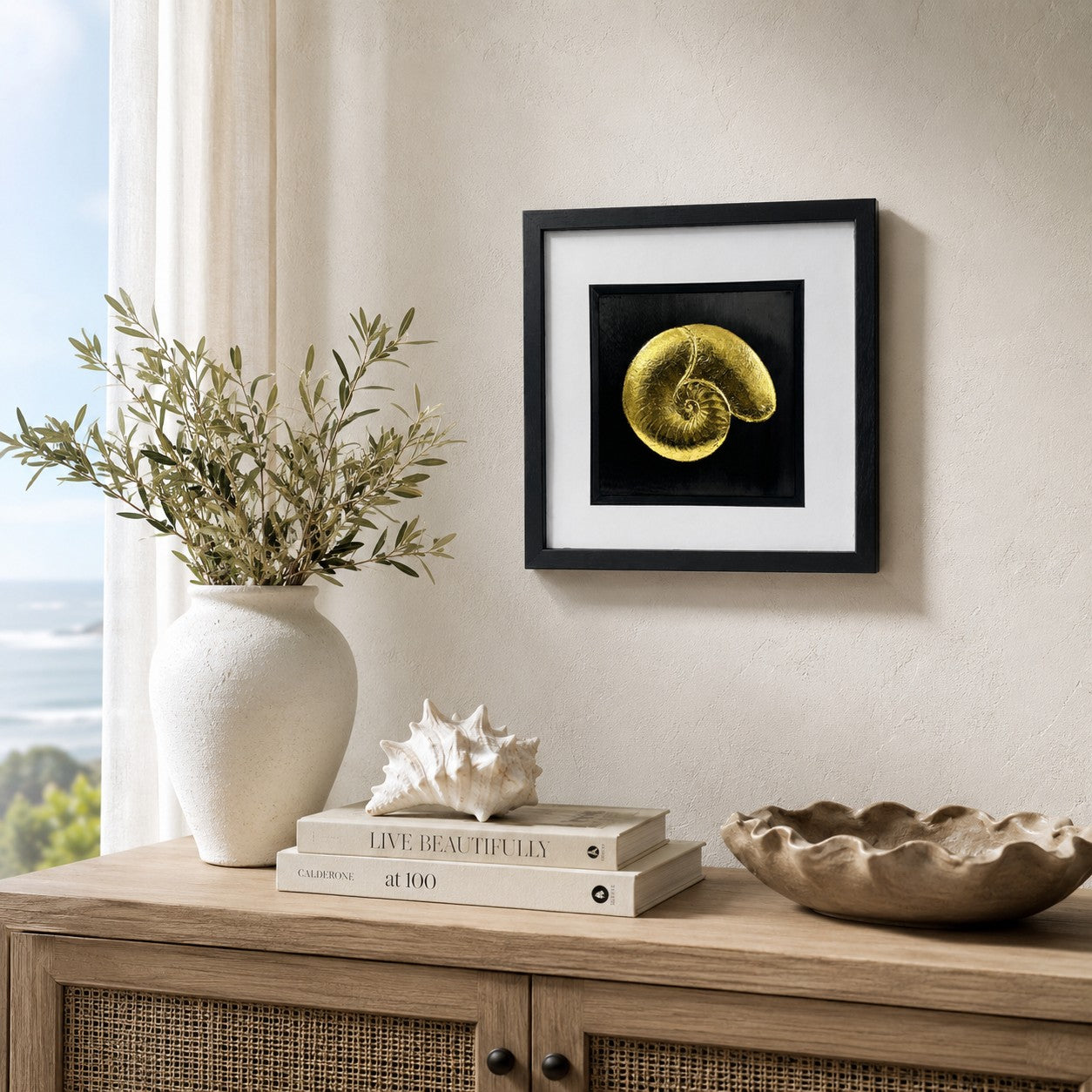 Gold nautilus shell wall art displayed in a coastal inspired interior, featuring a 33 cm square framed hand gilded gold leaf 3D relief shell design on a black background with neutral seaside decor.