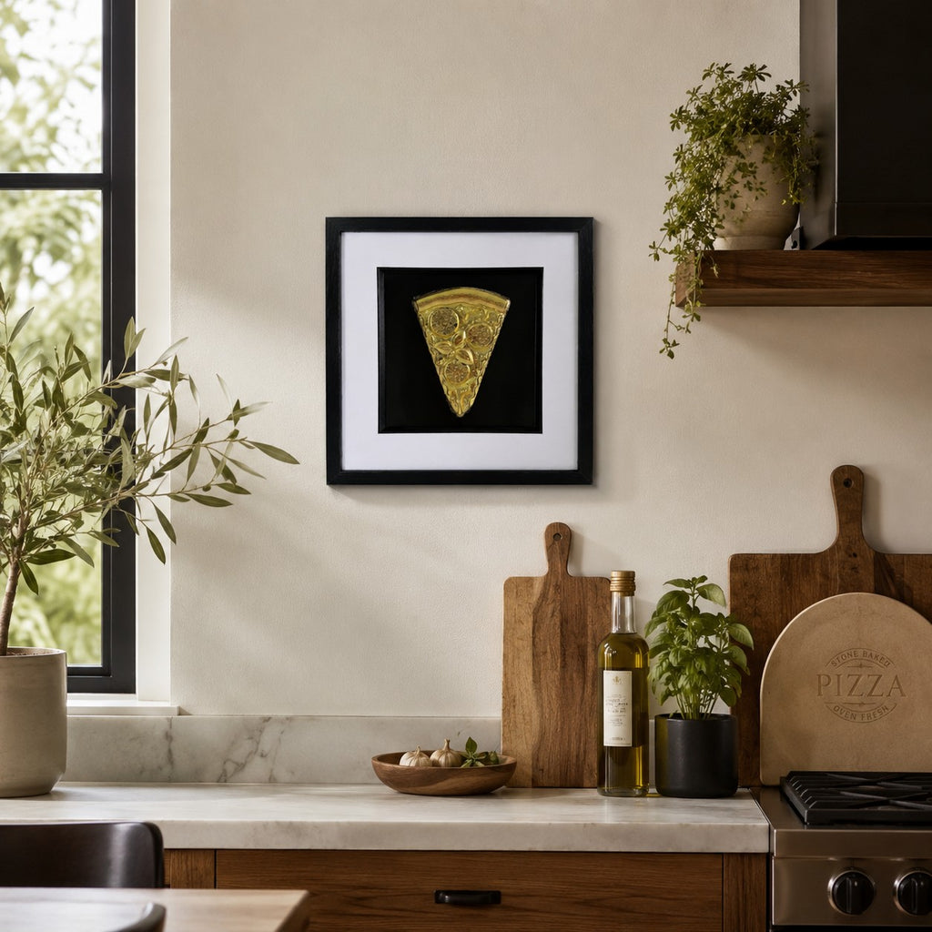 Gold 3D pizza slice artwork in black frame styled on a kitchen wall with wood boards, herbs and neutral decor.