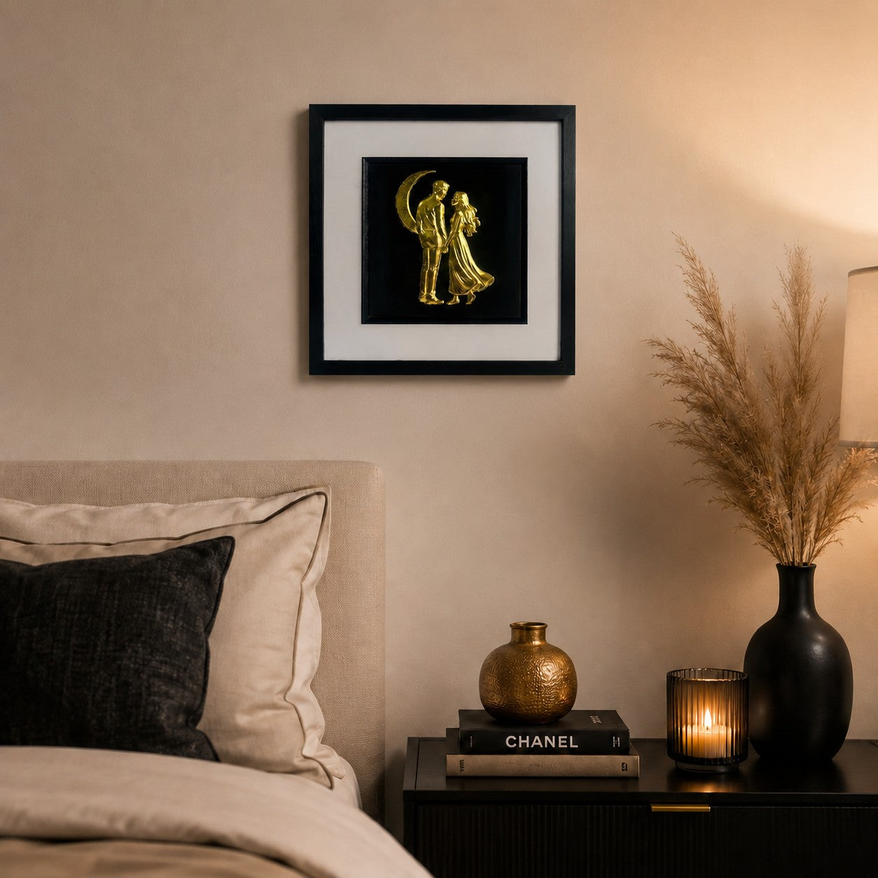 Gold romantic couple under the moon wall art displayed in a cosy bedroom, featuring a 33 cm square framed hand gilded gold leaf 3D relief design on a black background.