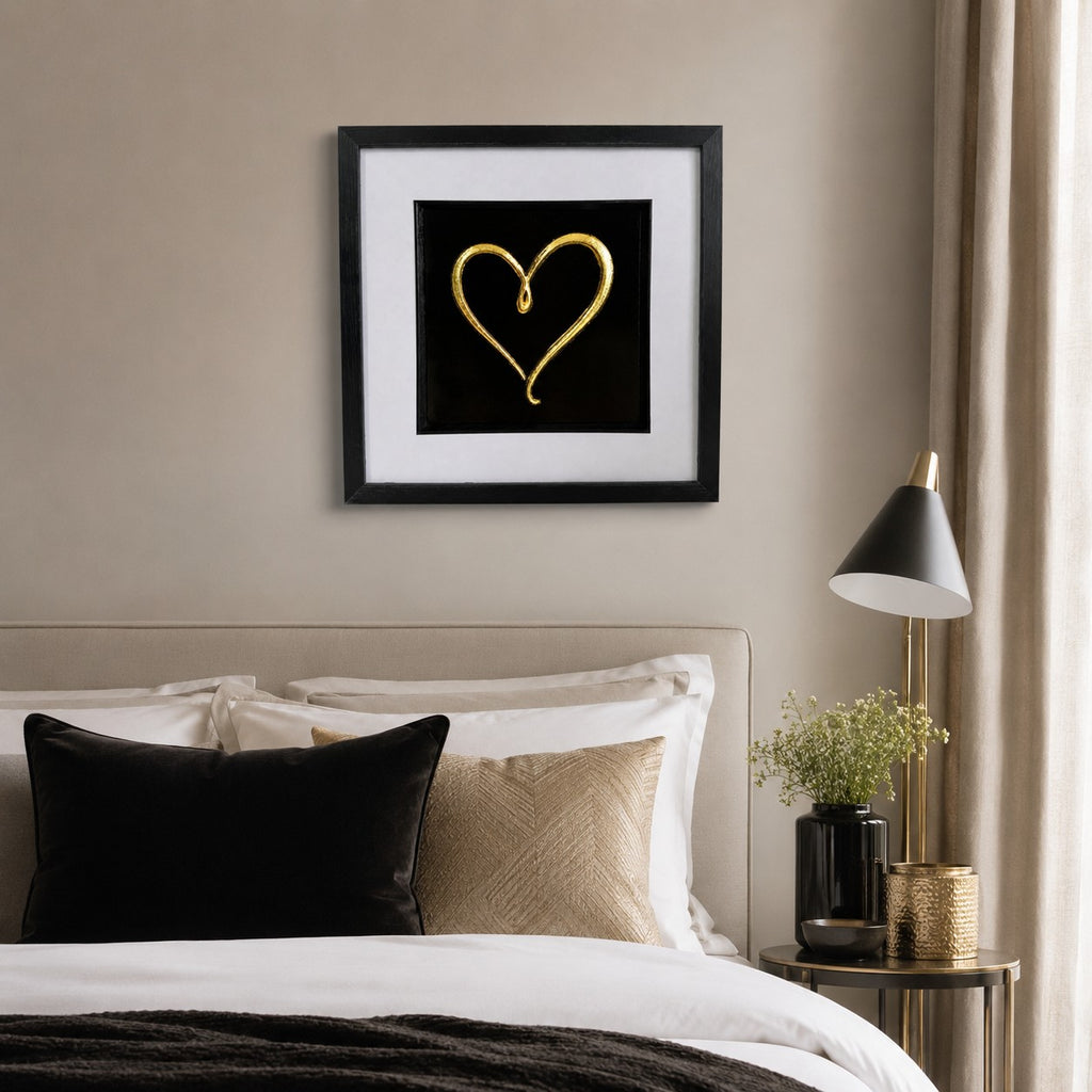 Gold love heart framed artwork above a bed with neutral bedding, black cushion and soft gold accents.