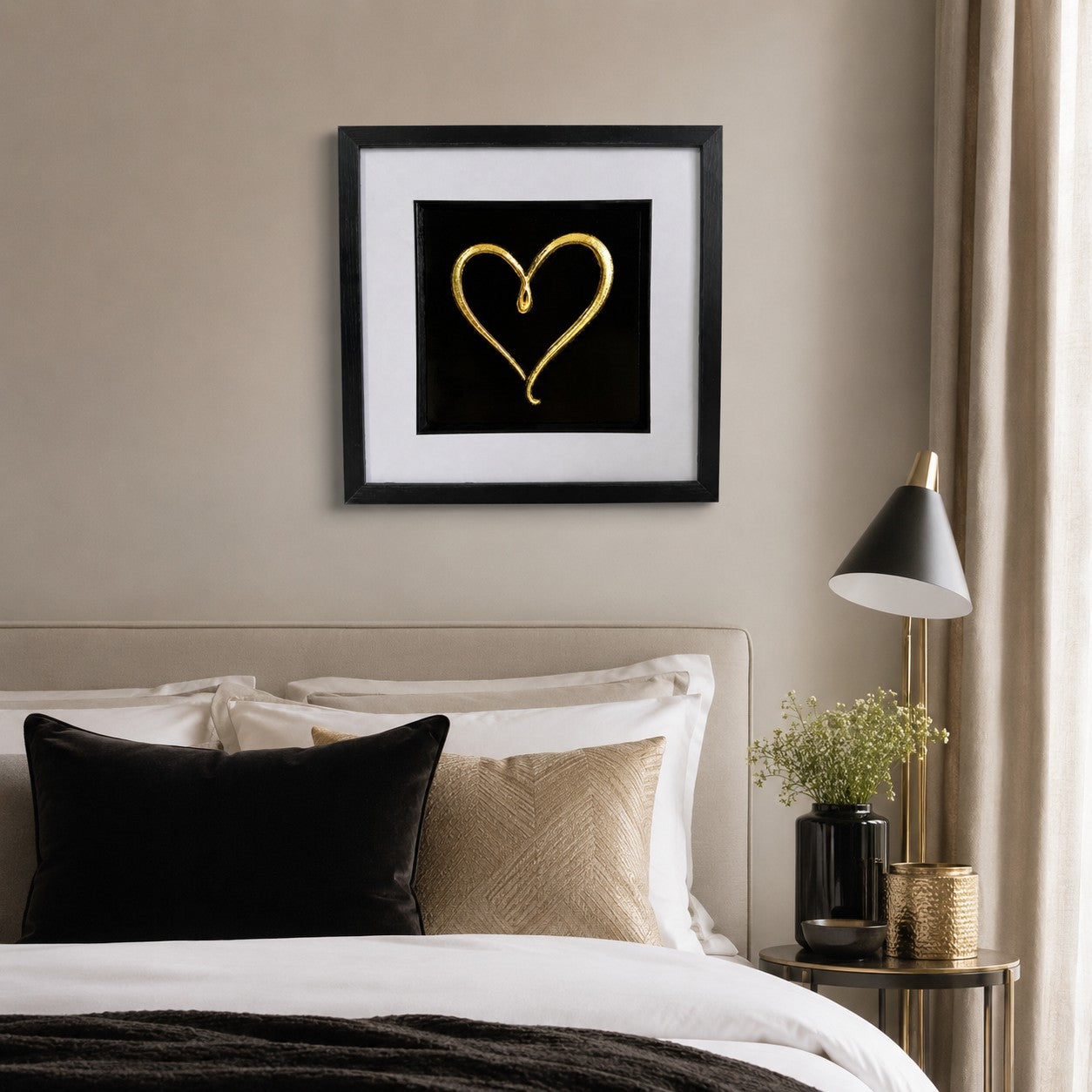 Gold love heart framed artwork above a bed with neutral bedding, black cushion and soft gold accents.