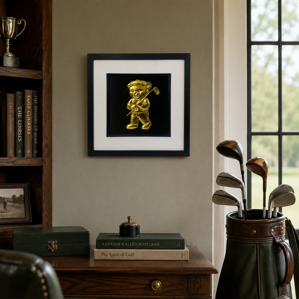 Gold teddy bear golfer wall art displayed in a golf inspired study, featuring a 33 cm square framed hand gilded gold leaf 3D relief teddy bear with golf club design on a black background.