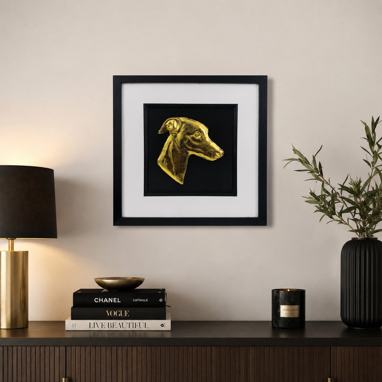 Gold whippet dog portrait wall art in a black frame with white mount, styled on a neutral wall above a dark wooden sideboard with luxury home decor.