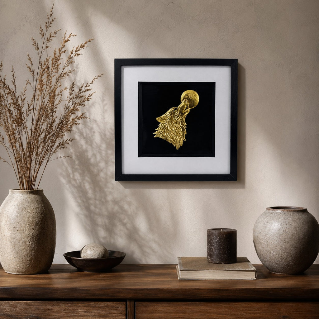 Gold wolf howling at the moon framed wall art displayed on a warm neutral wall above a wooden console with rustic natural decor and dried branches.