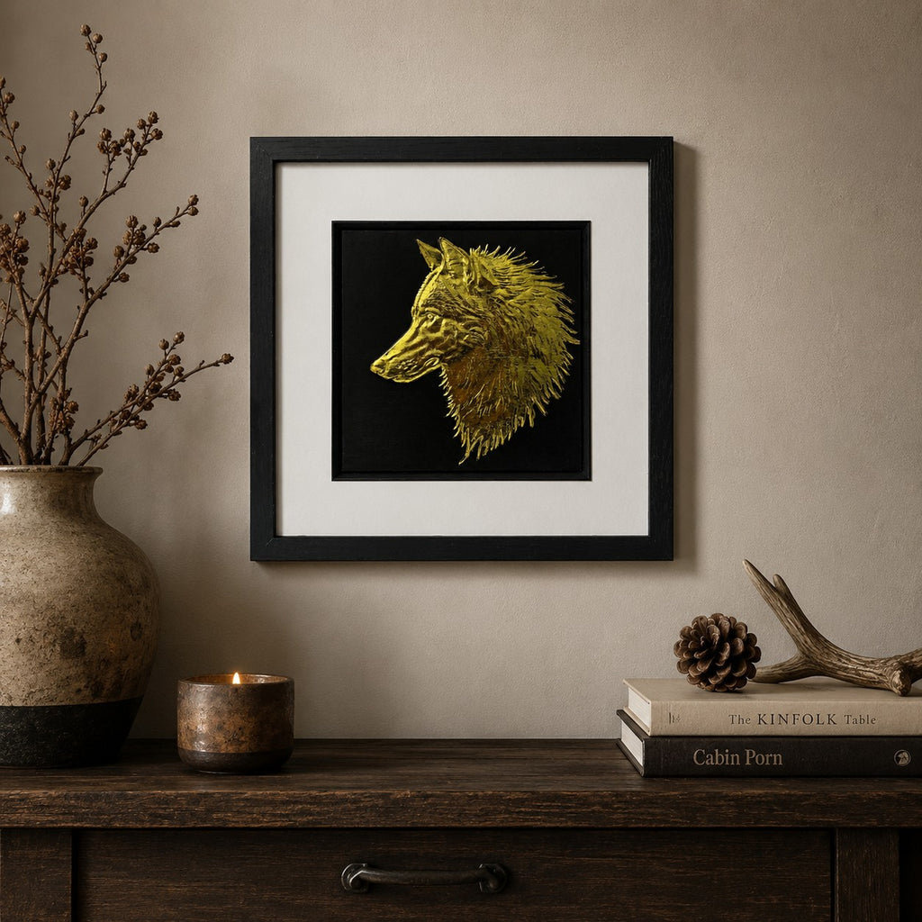 Gold wolf wall art in a black frame with white mount, styled on a neutral wall above a rustic wooden console with branches, candlelight, books, pinecone and antler decor.
