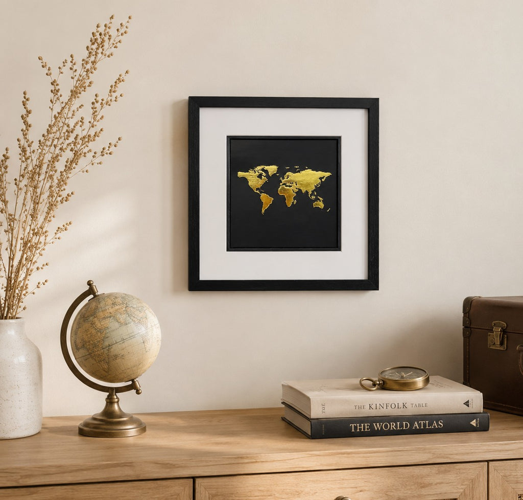 Gold world map wall art displayed in a travel inspired home interior, featuring a 33 cm square framed hand gilded gold leaf 3D relief map design on a black background.