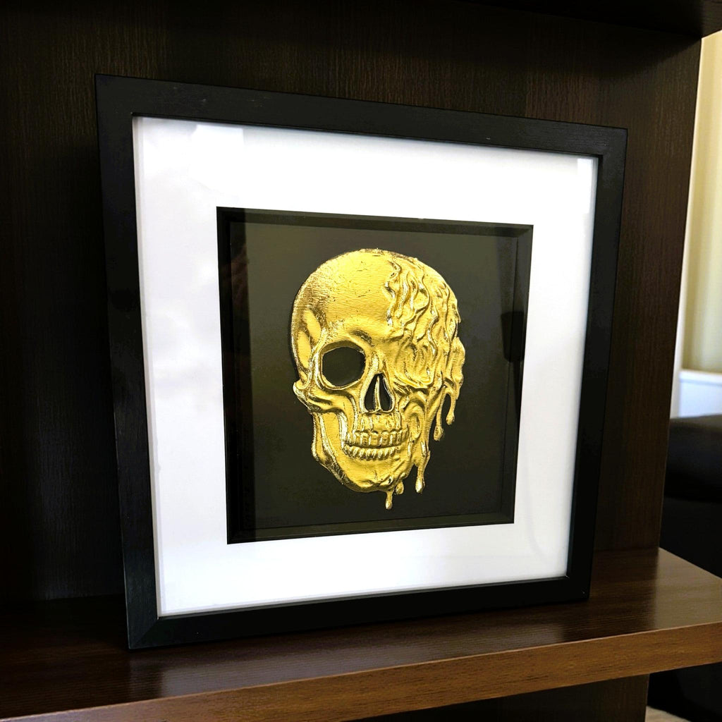 Styled shelf view of gold leaf molten dripping skull wall art in black frame
