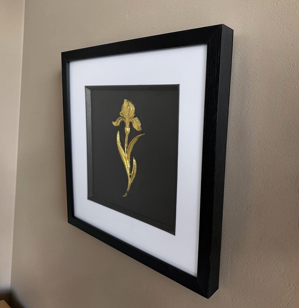 Angled side view of gold iris raised relief wall decor in a black frame on a neutral wall.
