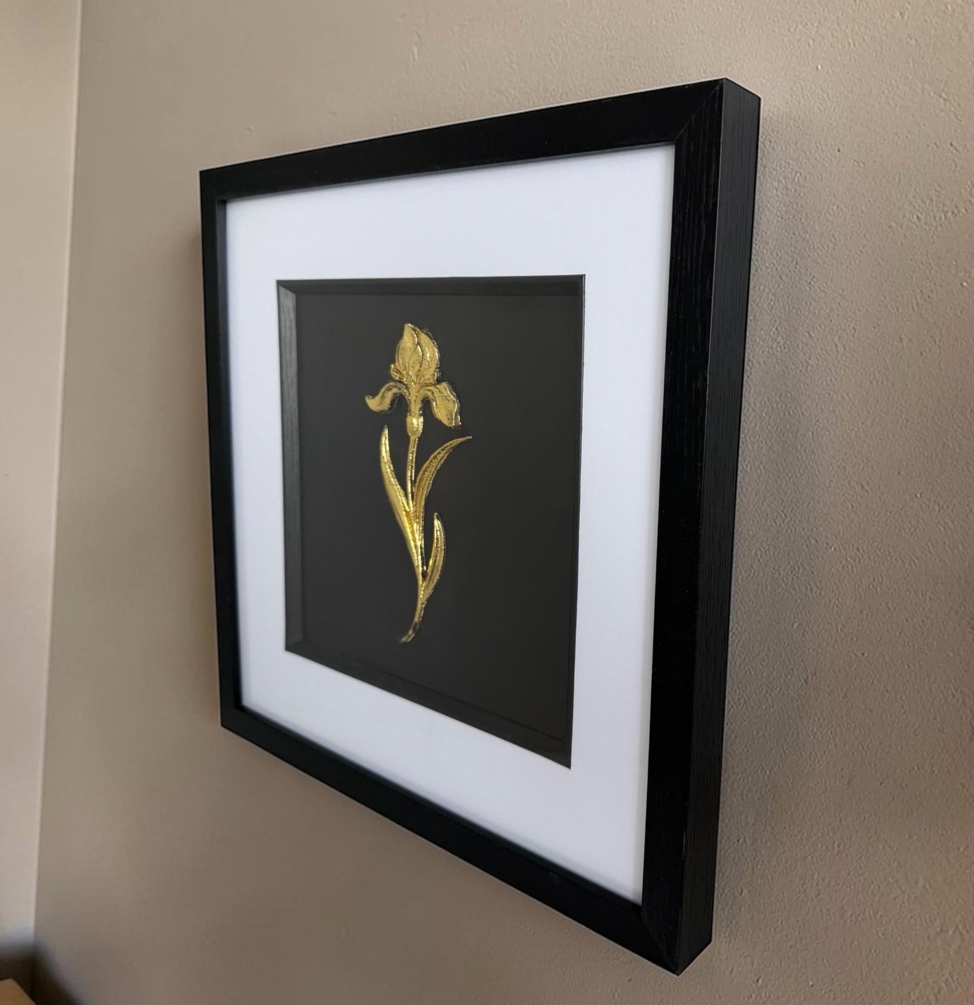 Angled side view of gold iris raised relief wall decor in a black frame on a neutral wall.