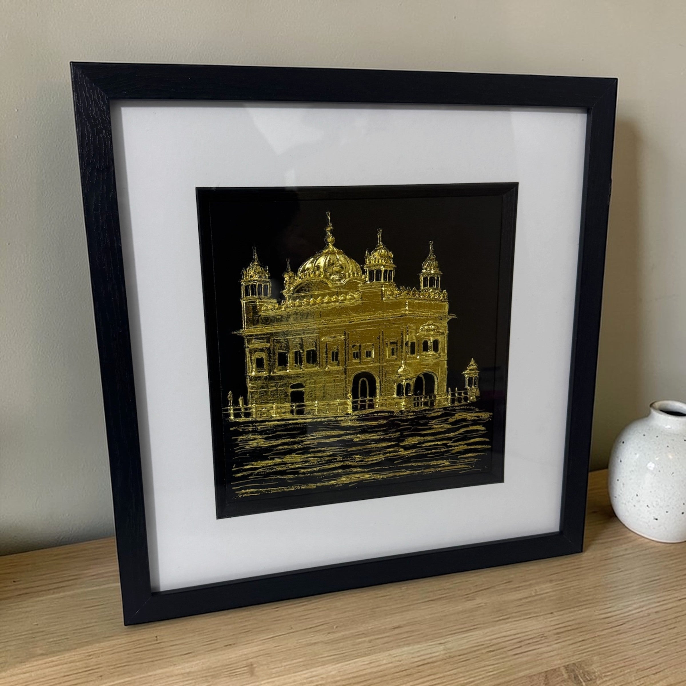 Angled view of Golden Temple wall art displayed on a shelf