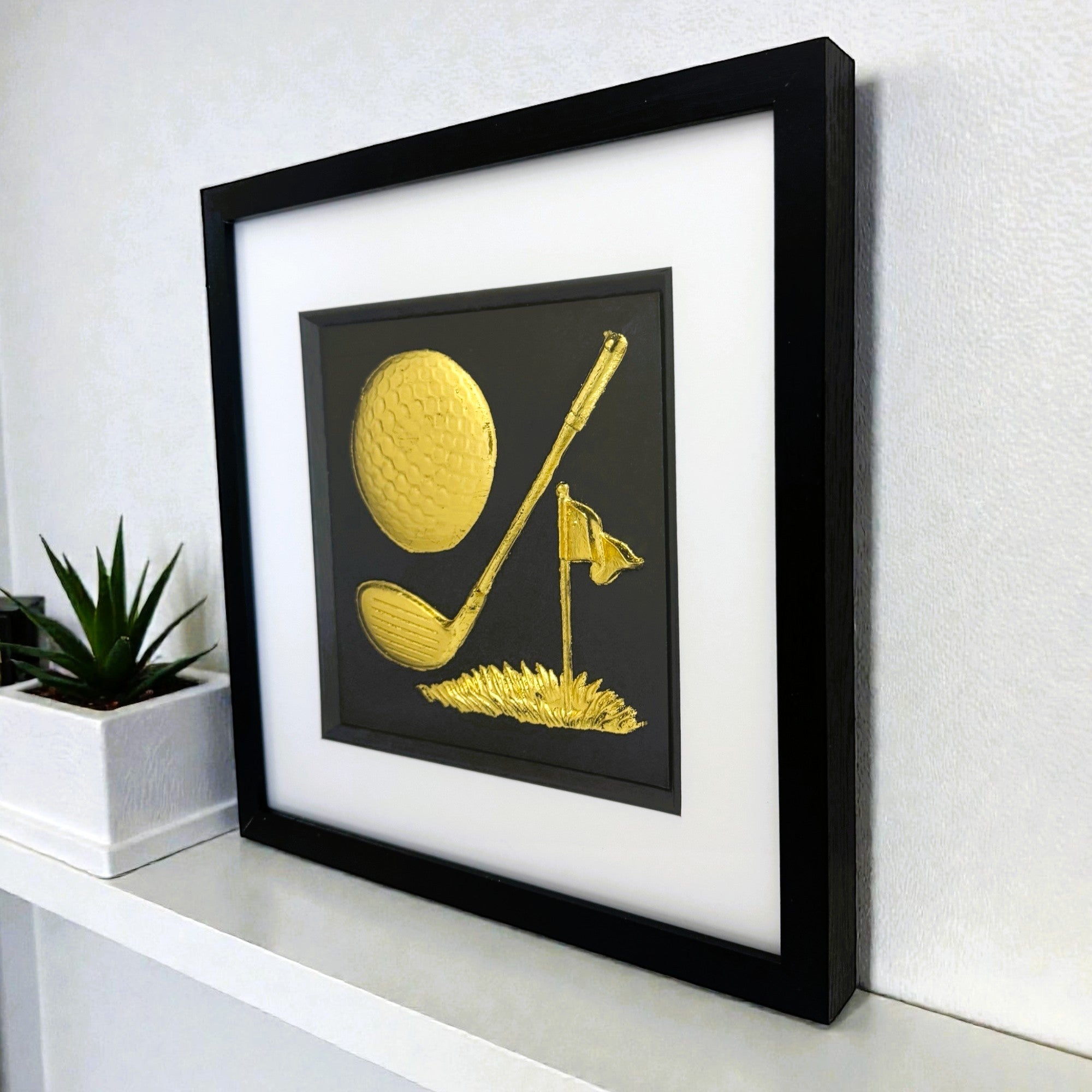 Framed gold golf theme 3D art displayed on white shelf.
