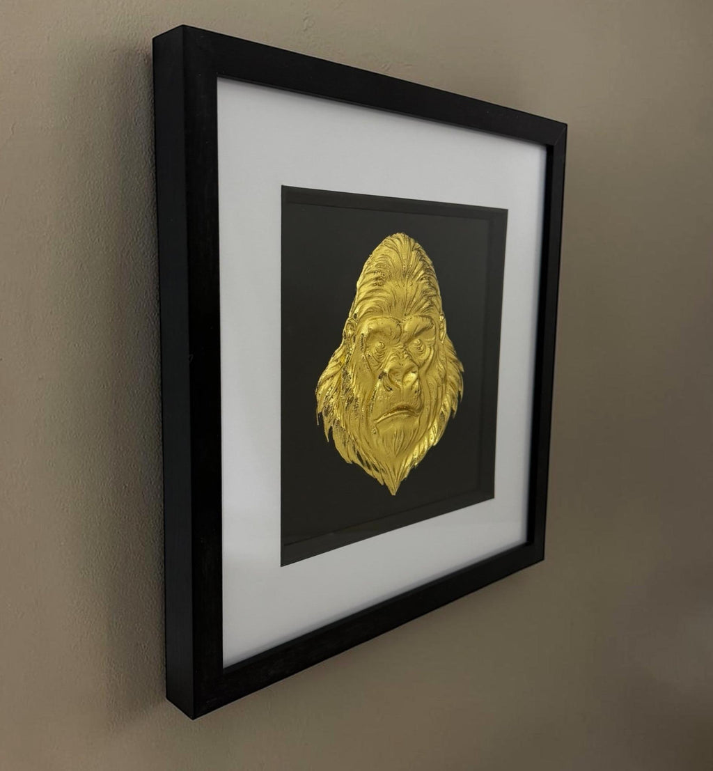 Gold framed gorilla head artwork on a neutral wall showing black box frame depth and glass front.