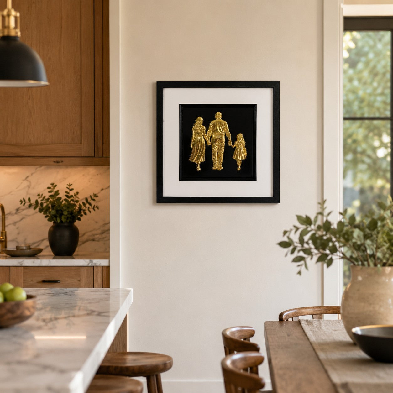 Gold 3D family relief artwork in black frame on kitchen wall, showing adult man, woman and child holding hands.