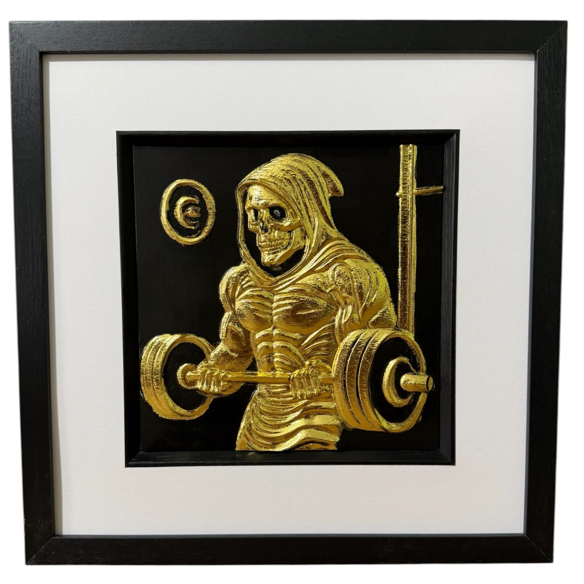 Framed grim reaper gym wall art, gold relief of a hooded skeleton lifting a loaded barbell, scythe propped behind him, on a black background in a black frame with white mount